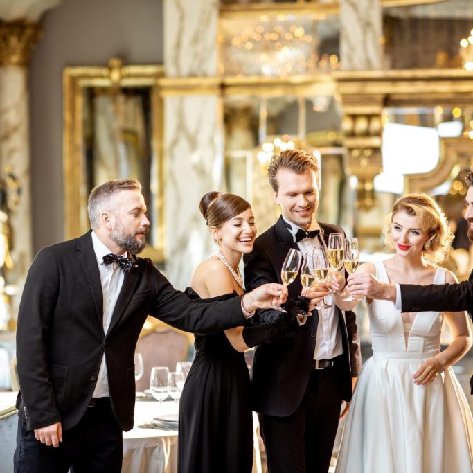Group of elegant people well-dressed in retro styles celebrating New Year holiday, having fun with wineglasses at the luxury restaurant hall